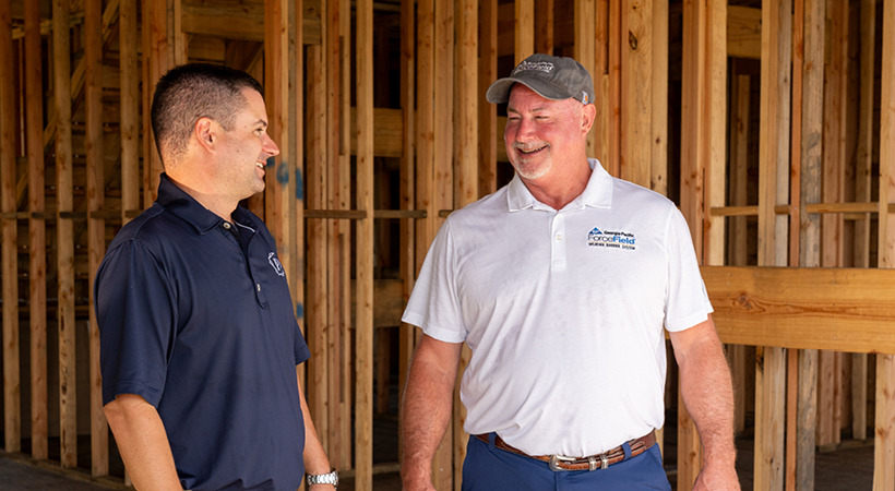 Landon Wright wears a blue polo and talks with Scott Collingwood, wearing a white polo, inside of a partially constructed home.