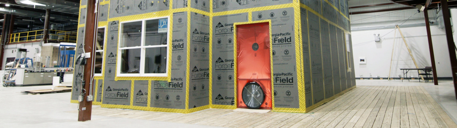 ForceField® Weather Barrier System is shown on a house inside a testing facility with a sealed blower door and fan showing. 