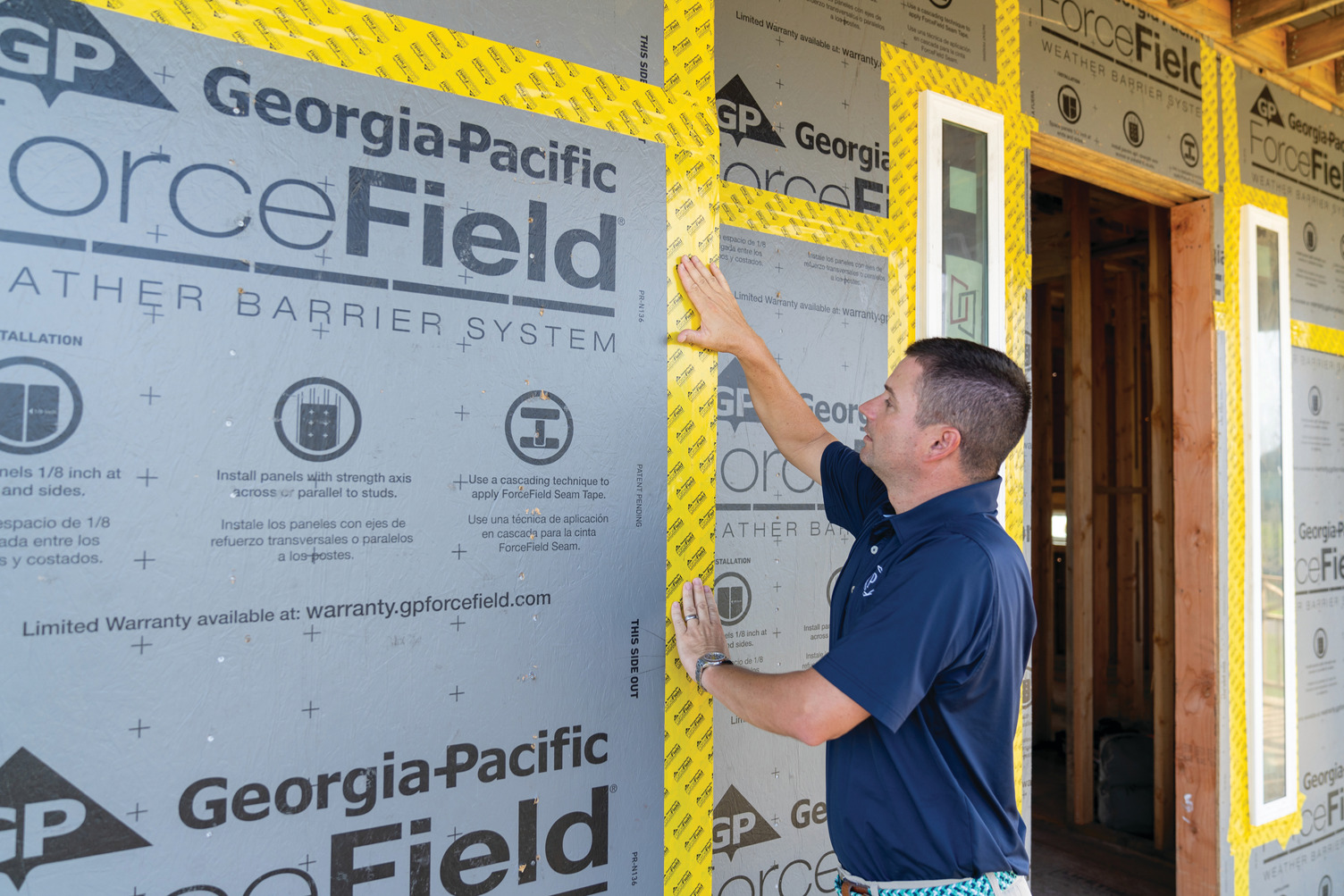 The owner of Prestige Custom Builders stands on the steps of a partially constructed home. He wears shorts and a blue polo.