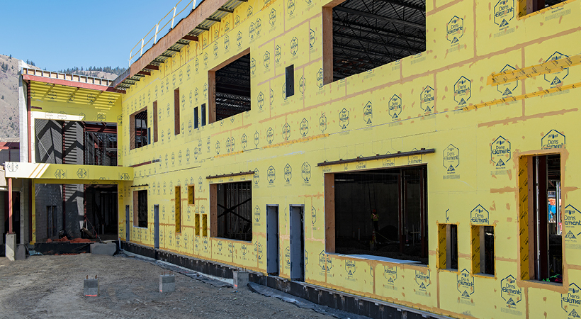 Construction workers wearing orange vests and hard hats are on an aerial lift installing bright yellow DensGlass® Sheathing on a building’s top floor.